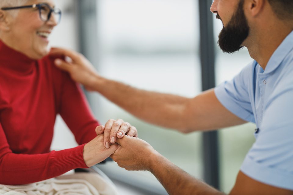 Cuidador segurando as mãos de uma senhora sorridente